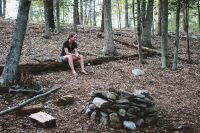 This tent site is nestled in the woods next to boulders and trees.